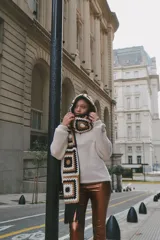 Bufanda tejida a mano en crochet, con capucha y diseño de cuadrados en tonos beige, marrón y negro.