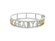 Pulsera rígida dorada con nombre calado y detalles de circonitas.