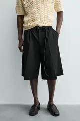 Bermuda negra de corte ancho (wide fit) con pliegues frontales, bolsillos laterales y bolsillos traseros de vivo.