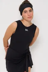 Vestido corto deportivo negro, sin mangas, con cuello redondo y detalle de lazo anudado en la cintura. Presenta el logo 'bk.' estampado en blanco en el pecho.