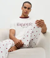 Pijama largo para hombre compuesto por una remera de manga corta blanca con cuello redondo bordó y estampa frontal de dados con la leyenda 'Lucky to Have You', y un pantalón largo blanco con estampado full print de corazones bordós y cintura elástica.