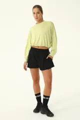 Buzo crop color verde claro, con cuello redondo y mangas largas holgadas. Presenta frunce en el ruedo mediante cordón elástico y tanca.