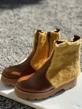 Botas de cuero marrón con la caña recubierta de corderito verde. Presentan una suela de plataforma tipo track en color beige y un tirador en la parte posterior para facilitar el calce.