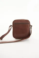 Morral bandolera de cuero genuino color marrón, con diseño compacto, cierre superior y correa ajustable para el hombro.