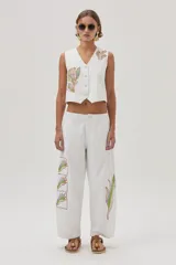 Chaleco blanco de gabardina con bordados florales y cierre frontal con botones forrados en la misma tela.