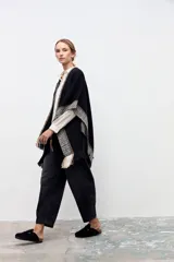 Ruana de tejido de punto en color negro, con diseño de guardas geométricas en tonos beige y blanco en los bordes y terminación con flecos.