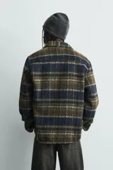 Sobrecamisa de corte relajado confeccionada en tejido con textura efecto pelo. Presenta diseño de cuadros en tonos verde y negro, cuello solapa, cierre frontal con botones, manga larga con puños abotonados y un bolsillo de plastrón en el pecho.