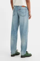 Jean de corte relajado y pierna cónica, con diseño de cinco bolsillos y cierre frontal con botones. Presenta un lavado azul claro con efecto desgastado, roturas localizadas y detalles de salpicaduras de pintura.