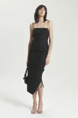 Vestido midi negro de breteles finos, confeccionado en gabardina liviana elastizada. Tiene calce entallado, recortes en el delantero, cierre invisible en la espalda y drapeado lateral en la falda. La espalda es descubierta con tiras cruzadas que se atan en la cintura.