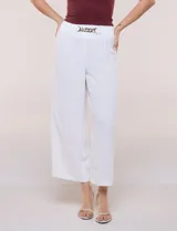 Pantalón negro de calce relajado y caída fluida, confeccionado en poliéster con textura de crepé. Tiene cintura alta elastizada estilo pull on con un aplique de cadena metálica decorativa, y pierna de corte ancho tipo wide leg corto por arriba del tobillo.
