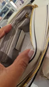 Cartera tipo bandolera de formato rectangular con estampado de cerezas sobre fondo claro. Cuenta con cierre superior, tirador con flecos y correa de tela ajustable y extraíble.