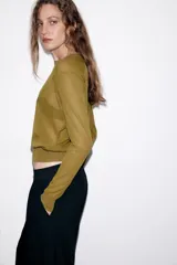 Jersey de punto fino con cuello redondo y manga larga con puños elásticos. Presenta un diseño minimalista con costuras visibles en los hombros.