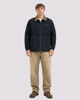 Campera estilo workwear de color azul oscuro, confeccionada en canvas resistente con interior de corderito sherpa. Presenta cuello de pana en color marrón, cierre frontal con botones metálicos color cobre, dos bolsillos frontales amplios y bordado de la marca en el pecho.