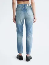 Jean de mezclilla azul claro con efecto lavado y zonas desgastadas/rotas en ambas piernas. Presenta un corte mom de talle alto, estilo clásico de cinco bolsillos y cierre de botón y cremallera.