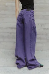 Jean de corte oversized y tiro medio-alto, confeccionado en denim de color violeta con diseño de cinco bolsillos y cierre frontal con botón y cremallera.