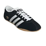 Championes Adidas modelo Tokyo, de diseño clásico y perfil bajo. Confeccionados en gamuza negra con las icónicas tres bandas laterales en cuero blanco y suela de goma color caramelo. Presenta el logo de la marca y el nombre del modelo en dorado en el lateral.