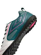 Championes de fútbol Umbro modelo Vision TF, diseñados para césped sintético. Presentan una combinación de colores blanco, verde azulado y detalles en fucsia, con el logo de la marca en el lateral y suela de goma con tapones pequeños.