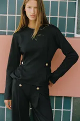 Pantalón de tiro alto con pierna ancha, confeccionado en sarga color tostado. Presenta detalle de doble hilera de botones metálicos dorados en el frente y pinzas verticales.