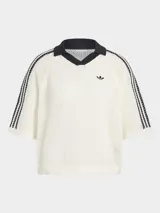 Polo de crochet color blanco con cuello polo negro en V, mangas cortas con las icónicas tres tiras de Adidas en negro y logo de la marca bordado en el pecho.
