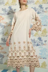Vestido midi de algodón color crudo, con corte holgado, mangas largas acampanadas y diseño con bordados calados de flores en color marrón en el ruedo y en las mangas.