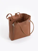 Cartera tipo shopper de cuero vacuno flor graneado, con formato amplio y estructura flexible. Presenta dos cierres verticales decorativos en el frente con tiracierres personalizados y doble manija de hombro.