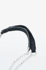Cartera negra de gamuza con tachas plateadas en el borde inferior y lateral. Tiene una correa de cadena plateada con un detalle de hombrera de gamuza.