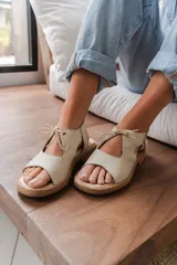 Sandalias de cuero color crudo, con tiras anchas sobre el empeine y ajuste con cordones finos.