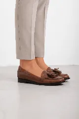 Mocasines de cuero marrón con diseño clásico, detalles de flecos y borlas en el empeine, y suela plana.