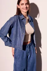 Camisa de jean azul de corte recto, con cuello clásico, cierre frontal con botones marrones, bolsillo de parche en el pecho y mangas largas con puños abotonados.