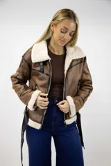 Campera estilo aviador de cuero sintético marrón con interior y detalles de corderito sintético en color crudo. Cuenta con cierre frontal metálico, detalles de tiras con hebilla en el cuello y el ruedo, y ribetes en color negro.