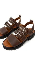 Sandalias de cuero color marrón chocolate, con tres tiras horizontales con ojales y hebillas metálicas plateadas. Suela de goma negra con plataforma.