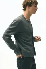 Cárdigan de punto fino color gris oscuro, con cuello en V pronunciado y cierre frontal de botones. Presenta un acabado ligeramente cepillado y puños y bajo acanalados.