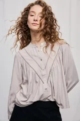 Blusa de manga larga con cuello mao y botonadura frontal. Presenta detalles calados en forma de V, frunces que aportan amplitud y mangas con volumen, logrando una silueta fluida y femenina.