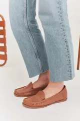 Mocasines de cuero color dorado con acabado texturizado, diseño clásico de punta redondeada y costuras visibles en el empeine. Cuentan con suela plana y flexible.