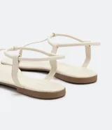 Sandalia plana de mujer color dorado metalizado, con diseño minimalista de tira fina que une la puntera y el empeine, y tira elástica fina alrededor del tobillo.