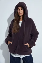 Canguro de corderito con capucha, cierre frontal y bolsillos laterales. Diseño relajado y textura suave.