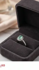 Anillo de plata 925 con piedra central ovalada de color verde claro, rodeada por un halo de pequeñas piedras brillantes y banda decorada con cristales.