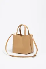 Bolso pequeño de piel vacuna color negro, con estructura rígida, doble asa de mano y correa larga ajustable para llevar al hombro o cruzado. Presenta cierre de botón a presión y logo metálico de la marca en el frente.