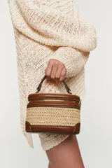 Bolso tipo vanity combinado en rafia y efecto cuero marrón, con cuerpo de tejido trenzado, detalles de pespuntes, asa de mano superior y cierre de cremallera.