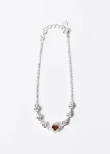 Pulsera plateada con cadena de eslabones y dije central con una zirconia roja rodeada de pequeñas circonias blancas.