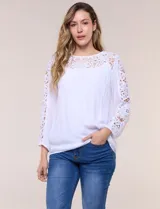 Blusa blanca de gasa liviana con forro interno en el cuerpo, de estilo boho-chic y silueta semi holgada. Presenta escote redondo con canesú de encaje calado en el frente y mangas largas con paneles longitudinales de encaje.