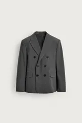 Blazer de corte relaxed fit color gris, confeccionado en tejido con lana. Cuenta con solapas de pico, manga larga con botones en los puños, bolsillos con solapa en la cadera y un bolsillo de vivo en el pecho. Presenta cierre frontal de botonadura cruzada con botones oscuros.