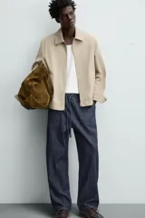 Cazadora color beige de algodón, corte recto, con cuello solapa, cierre frontal con cremallera, manga larga con puños abotonados y bolsillos laterales de ojal.