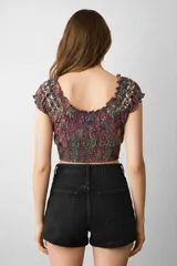 Top corto ajustado al cuerpo, con escote profundo en V con volados, mangas cortas abullonadas y elástico fruncido en la base. Presenta un estampado floral en tonos morados, azules y verdes.