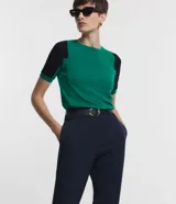 Blusa de viscosa con cuello redondo y mangas cortas. Presenta un diseño de bloques de color contrastantes, con cuerpo en tono malva y mangas en color negro, destacando por sus recortes asimétricos en la sisa.