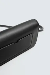 Bandolera negra con correa fina ajustable, cierre con solapa imantada, bolsillo interno y detalle de borla lateral.