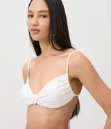 Top de bikini blanco con diseño de media taza, breteles finos y detalle de aplique frontal con forma de concha.