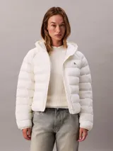 Campera puffer ligera Calvin Klein de color blanco, con diseño acolchado horizontal, capucha integrada y cierre frontal con cremallera. Presenta el logo de la marca bordado en el pecho.