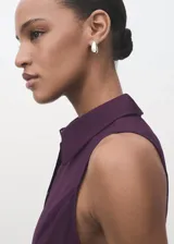 Vestido midi de corte evasé en color violeta oscuro, con cuello camisero, sin mangas y cierre frontal con botones. Incluye un cinturón ajustable a tono que marca la cintura.