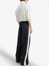 Pantalón negro de silueta relajada con pliegues frontales, cintura elástica y cierres metálicos largos en las piernas que revelan una apertura regulable y paneles laterales blancos.